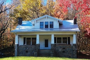 A two-story house with a stone foundation, a front porch, and a metal roof.