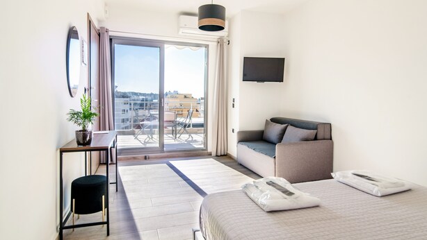Quarto de hotel moderno com cama, sofá, escrivaninha e uma ampla janela com vista para a cidade.