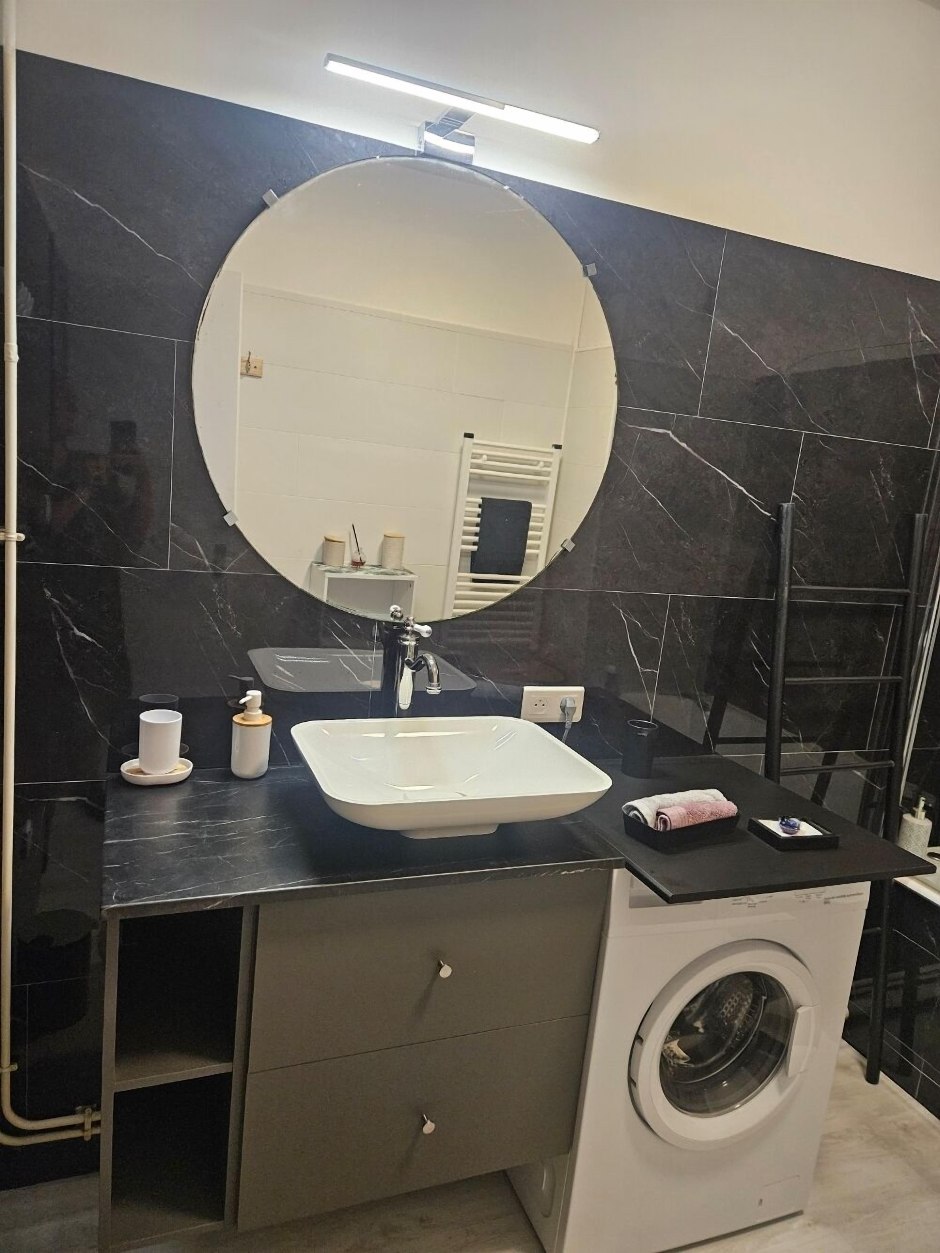 Une salle de bain moderne avec un grand miroir, un lavabo, un lave-linge et un porte-serviettes.