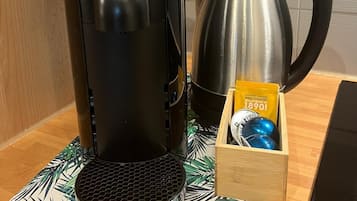 Een Nespresso koffieapparaat op een houten aanrecht, met een koffiekan en een doos Nespresso capsules.