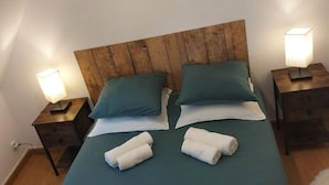 Una cama bien hecha con cabecera de madera, dos almohadas y dos lámparas de noche.