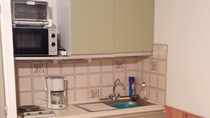 Una cucina compatta con forno a microonde, tostapane e macchina del caffè. Si trova un lavandino con rubinetto, un piccolo frigorifero e un tavolo in legno con sedie.