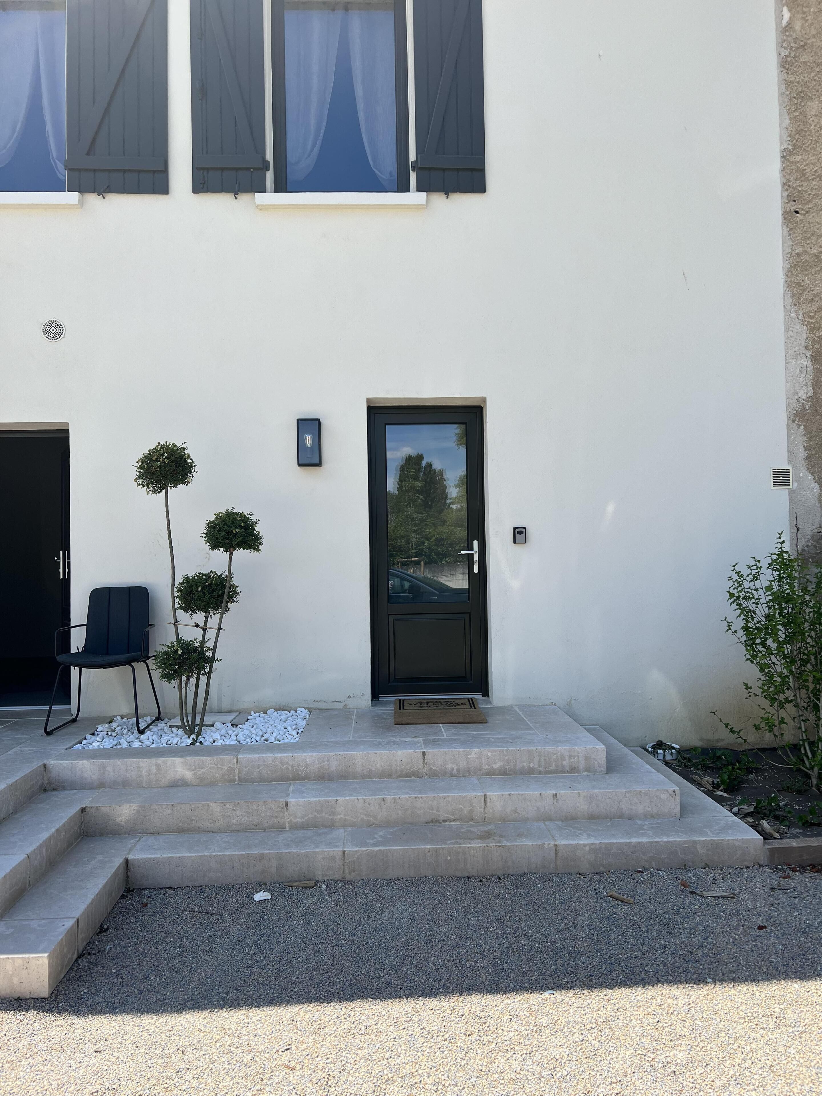A building with a black door, a small outdoor seating area with a chair, and a few potted plants.