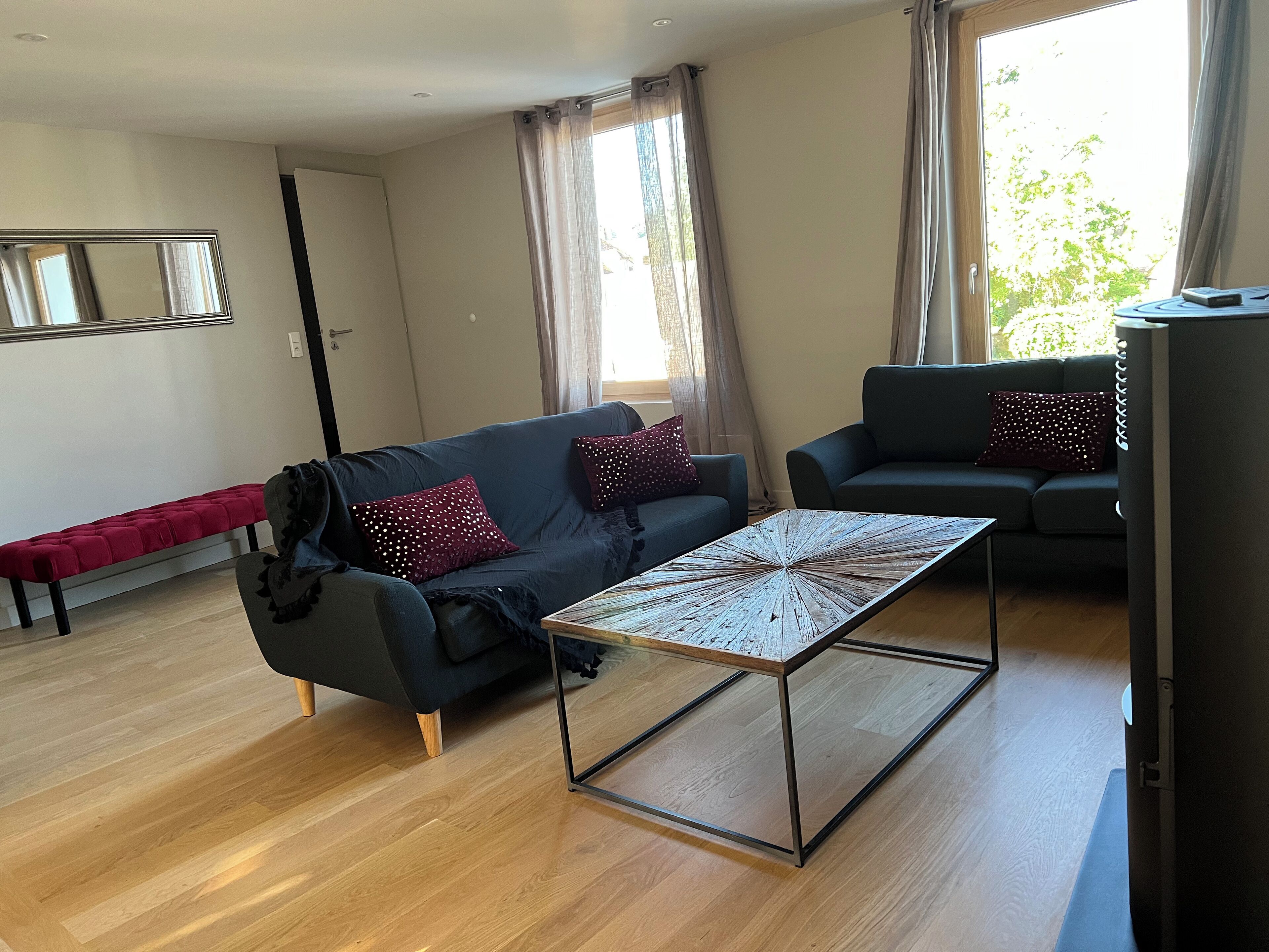 Una sala de estar moderna con un sofá azul oscuro, un banco rojo y una mesa de centro de vidrio.