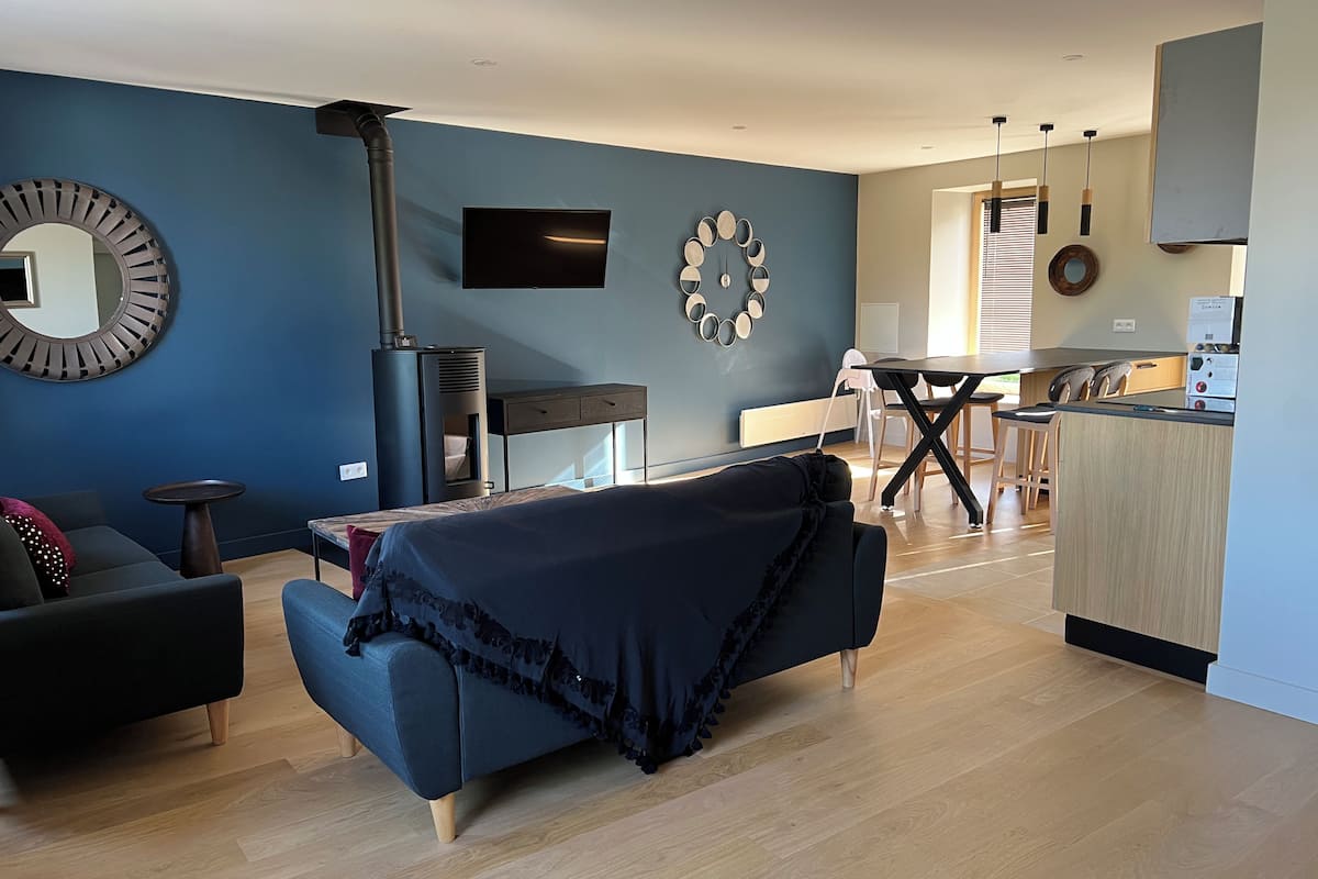 A modern living room with a sofa, a TV, a fireplace, and a kitchen area with a dining table and chairs.