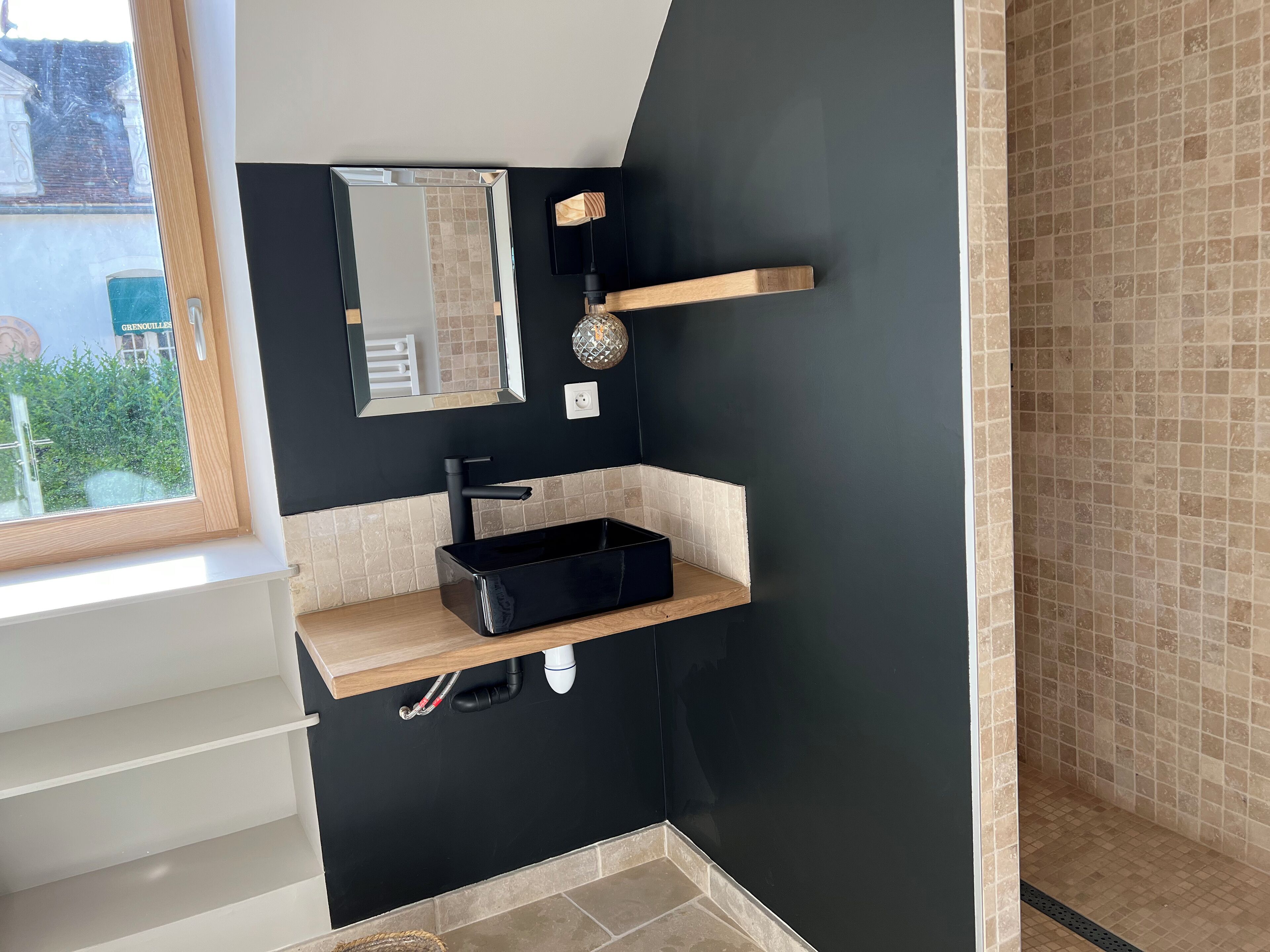 A modern bathroom with a black sink, a mirror, and a shower area.