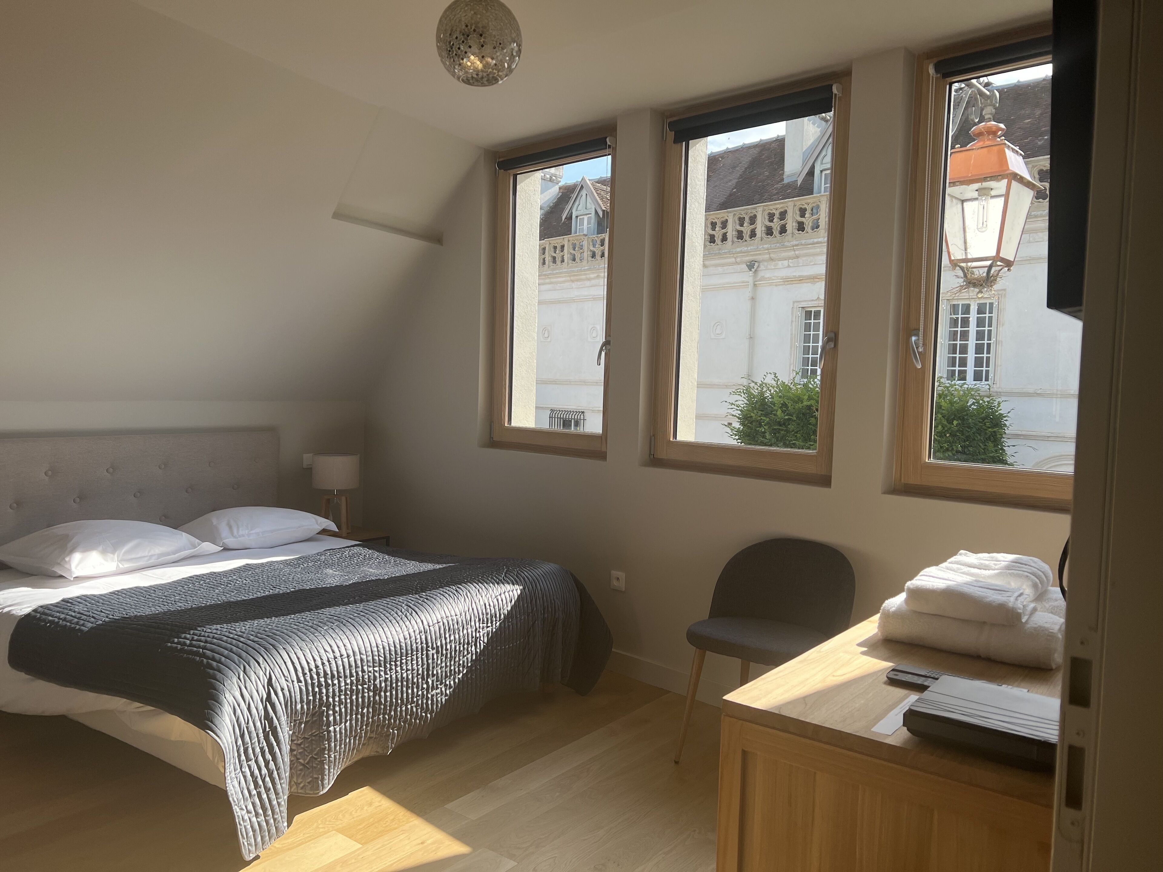 A bedroom with a bed, a chair, a desk, and a window with a view of buildings.