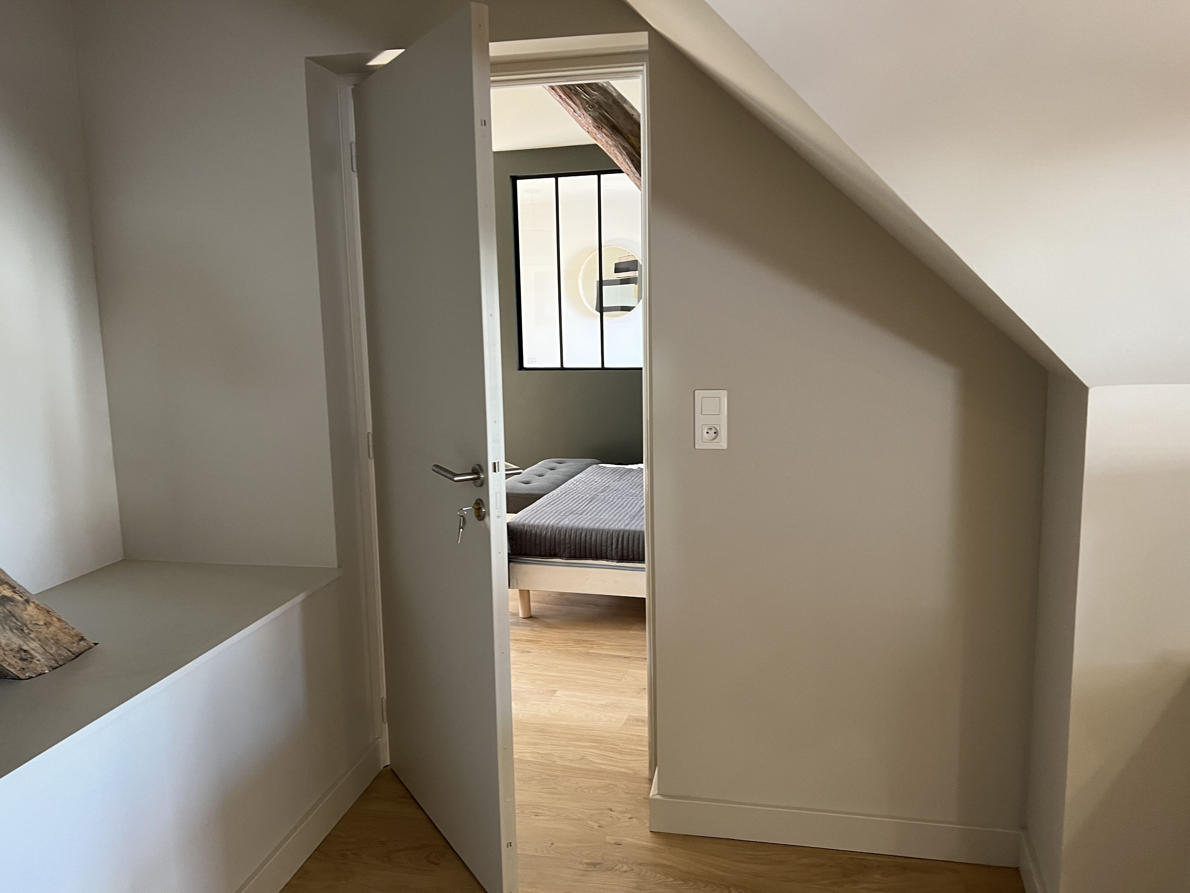 Un couloir étroit mène à une chambre à coucher qui contient un lit et une fenêtre.