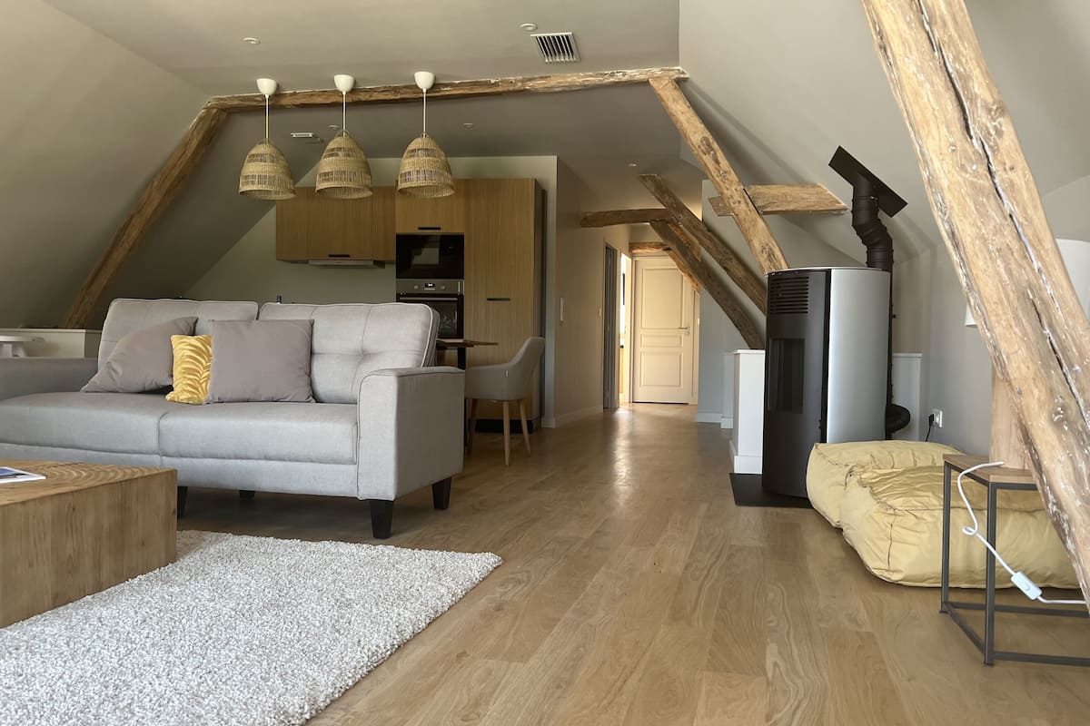 A modern loft-style living space with exposed wooden beams, a grey sofa, and a dining area.