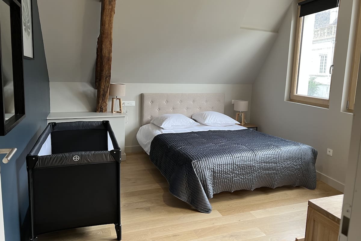 A bedroom with a bed, bedside tables, a lamp, a chair, a window, and a wooden beam.