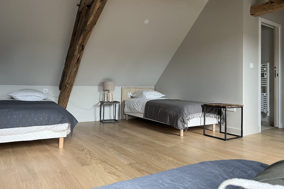 A bedroom with two beds, a small table, a lamp, and a wooden ceiling beam.