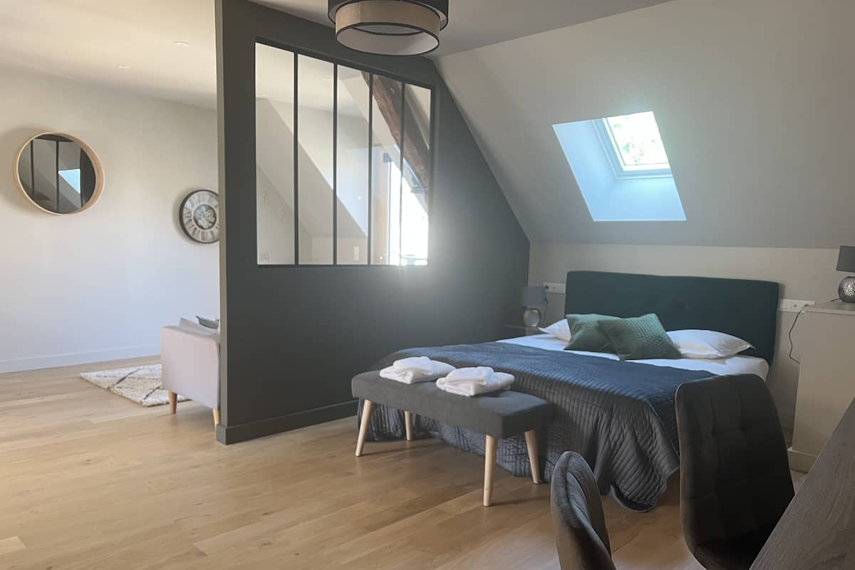 A modern bedroom with a skylight, a bed with pillows, a bench, and a round mirror on the wall.
