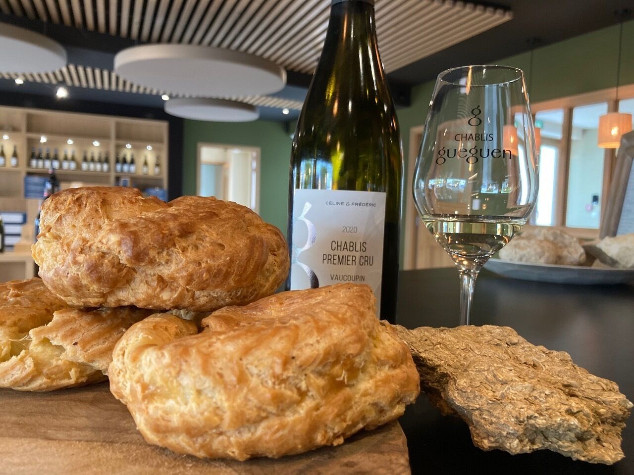 Una botella de vino Chablis Premier Cru, una copa de vino blanco y varios pasteles sobre una mesa de madera en un restaurante.