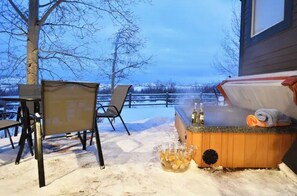 An outdoor seating area with a hot tub, chairs, and a table with bottles and glasses.