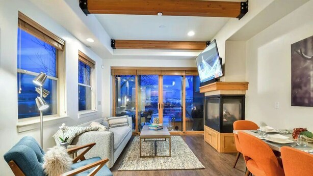 A modern living room with a fireplace, a television, and a dining area with orange chairs. - skiNewpark33: Walkable w/View, Deck, Hot Tub, Garage (Park City)