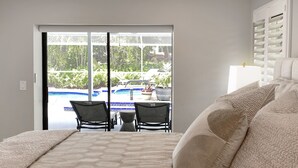 A bedroom with a large bed, two chairs, a small table, and a view of a swimming pool through a sliding door. - Newly Renovated, Beach Close, Pet Friendly, Modern Luxury Retreat (Naples)