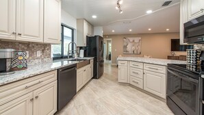 A modern kitchen with white cabinetry, a granite countertop, stainless steel appliances, and a large island with a sink. - Newly Renovated, Beach Close, Pet Friendly, Modern Luxury Retreat (Naples)