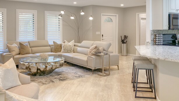 A modern living room with a sectional sofa, a glass coffee table, and a kitchen area with a bar. - Newly Renovated, Beach Close, Pet Friendly, Modern Luxury Retreat (Naples)