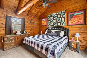 A wooden cabin bedroom with a bed, dresser, and quilted wall art.
