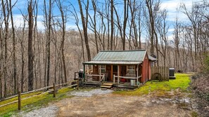 A rustic cabin with a metal roof, surrounded by a wooden deck and a gravel path.