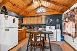 A kitchen with wooden cabinets, a refrigerator, a stove, and a dining table with chairs.