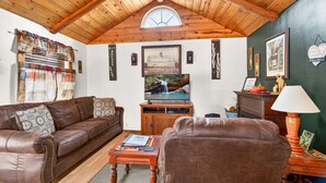 Una sala de estar acogedora, con techo de madera, un sofá de cuero marrón, una mesa de centro de madera y un televisor.