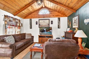 A cozy living room with a wooden ceiling, a brown leather sofa, a wooden coffee table, and a television.