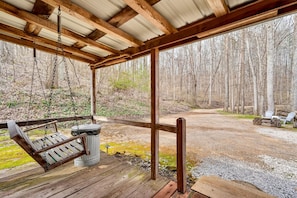 A wooden deck with a swing, a trash can, and a view of a forested area.