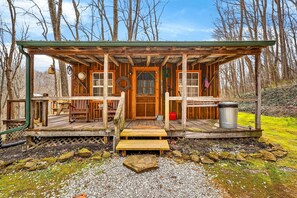 A rustic cabin with a wooden porch, a front door, and a small table and chair set outside.