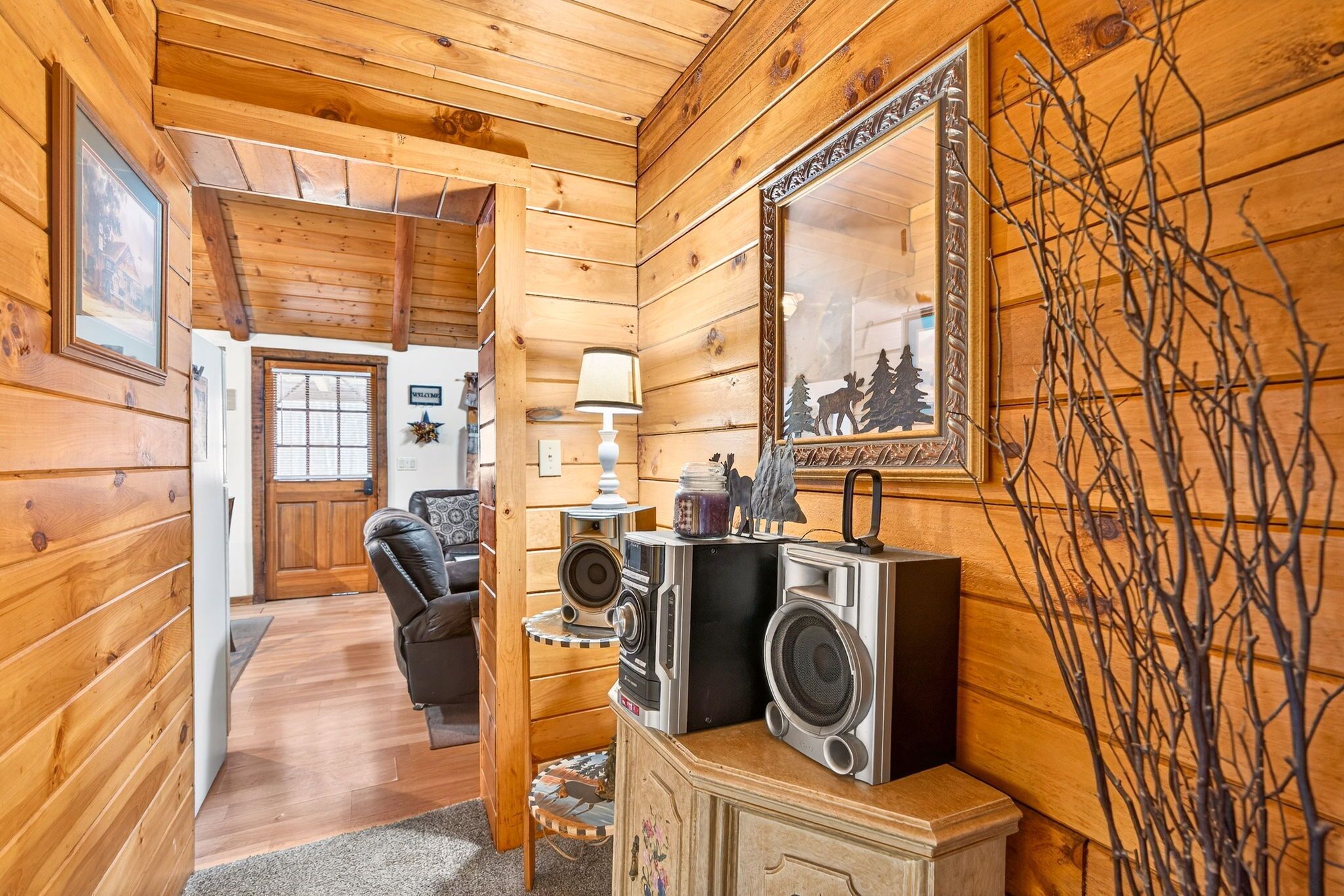 A wooden interior with a sofa, a lamp, a mirror, and a speaker setup.
