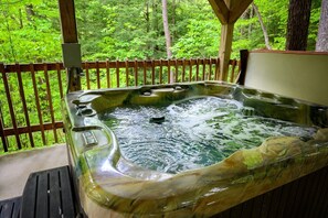 Un bain à remous avec une terrasse en bois et une vue sur une forêt.
