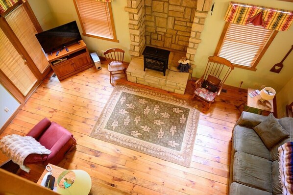 A cozy living room with a fireplace, wooden flooring, a sofa, a red armchair, and a television.