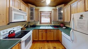 Une cuisine de taille réduite, dotée de meubles de rangement en bois, d’une cuisinière, d’un four à micro-ondes, d’un évier et d’un réfrigérateur.