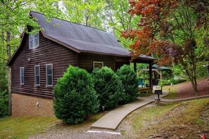 A rustic wooden cabin with a porch, surrounded by lush greenery and trees.