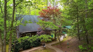 A house surrounded by dense trees, a covered porch, and a pathway leading to the entrance.