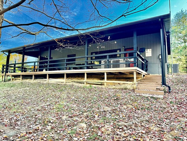 A building with a covered porch, a staircase, and a grassy area with fallen leaves. - Lazy Lane Cabins - Blue Jay (South Bloomingville)