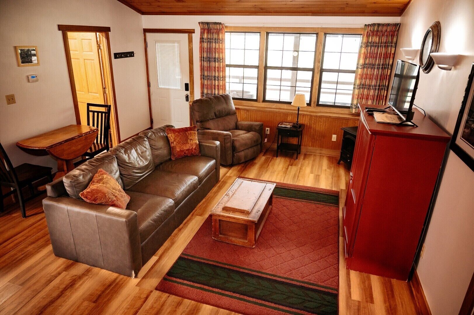 A living room with a brown leather sofa, a wooden coffee table, a red cabinet, and a television.