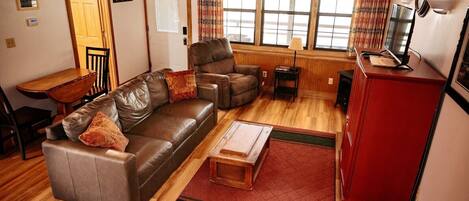 A living room with a brown leather sofa, a wooden coffee table, a red cabinet, and a television.