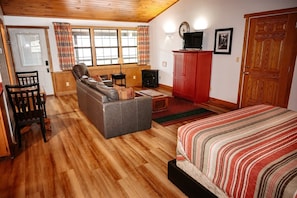 A cozy room with a sofa, a bed, a wooden floor, a red cabinet, and a window with curtains. - Lazy Lane Cabins - Blue Jay (South Bloomingville)