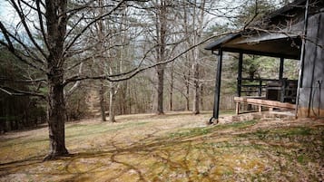 A rustic cabin with a covered porch and a picnic table, surrounded by a forested area.