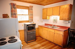 Cocina compacta con armarios de madera, microondas integrado, lavamanos y estufa.
