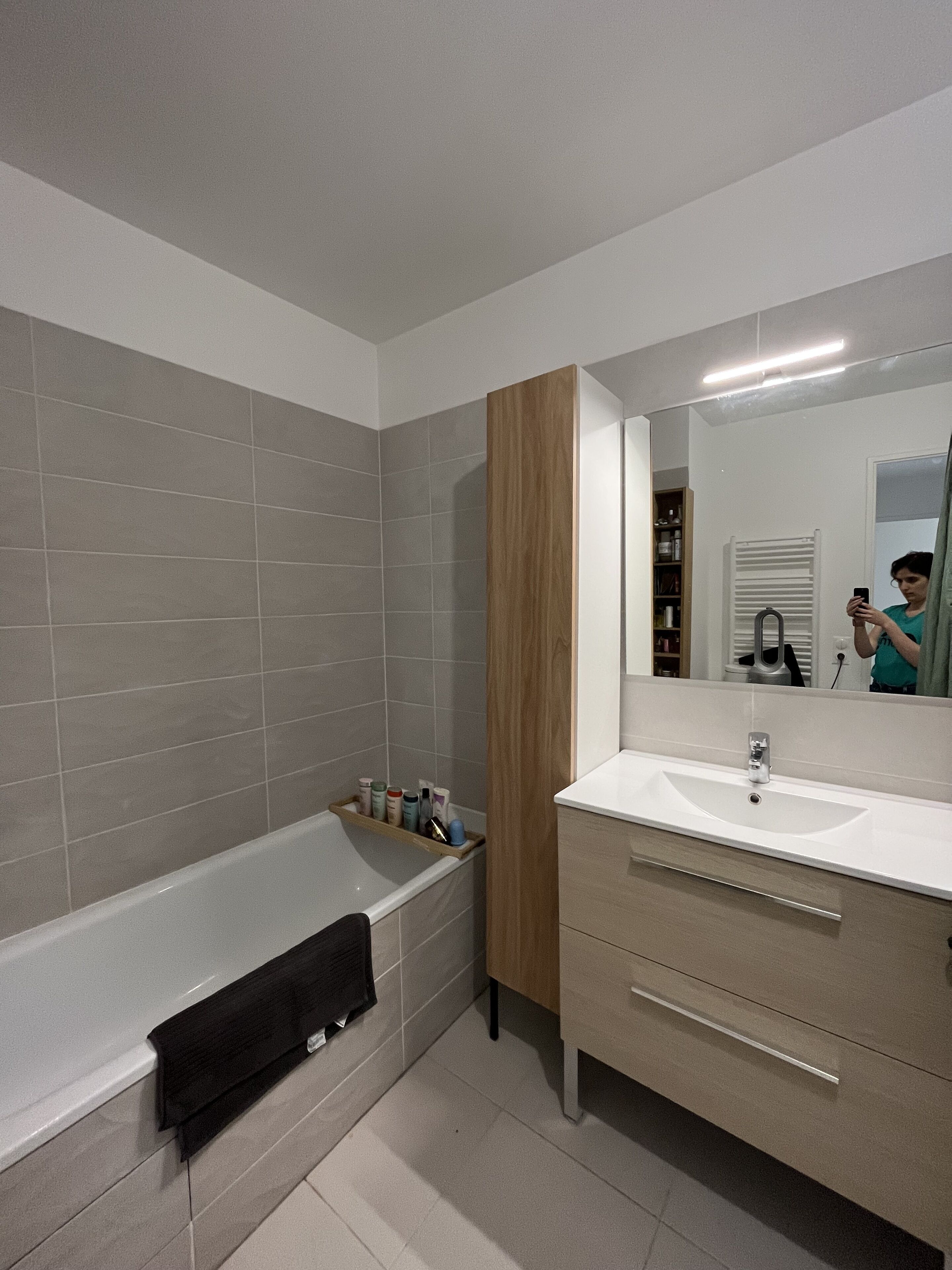 A modern bathroom with a bathtub, a vanity with a mirror, and a shelf with toiletries.