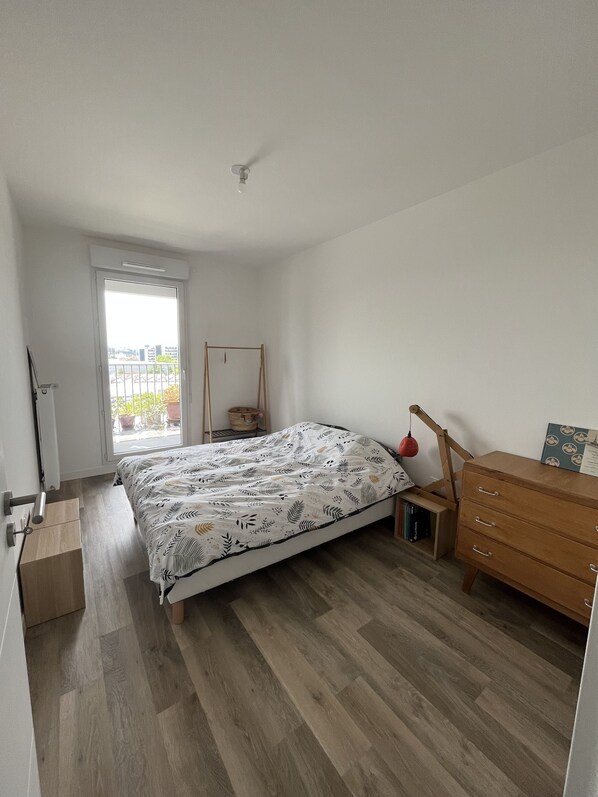 Un dormitorio con cama, cómoda de madera y ventana con vista a edificios.