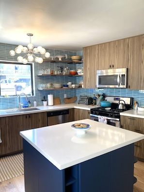 A modern kitchen with a central island, wooden cabinets, a stainless steel microwave, and a blue tiled backsplash. - Updated Mid-Century beach house --10 minute walk to the beach (Carlsbad)