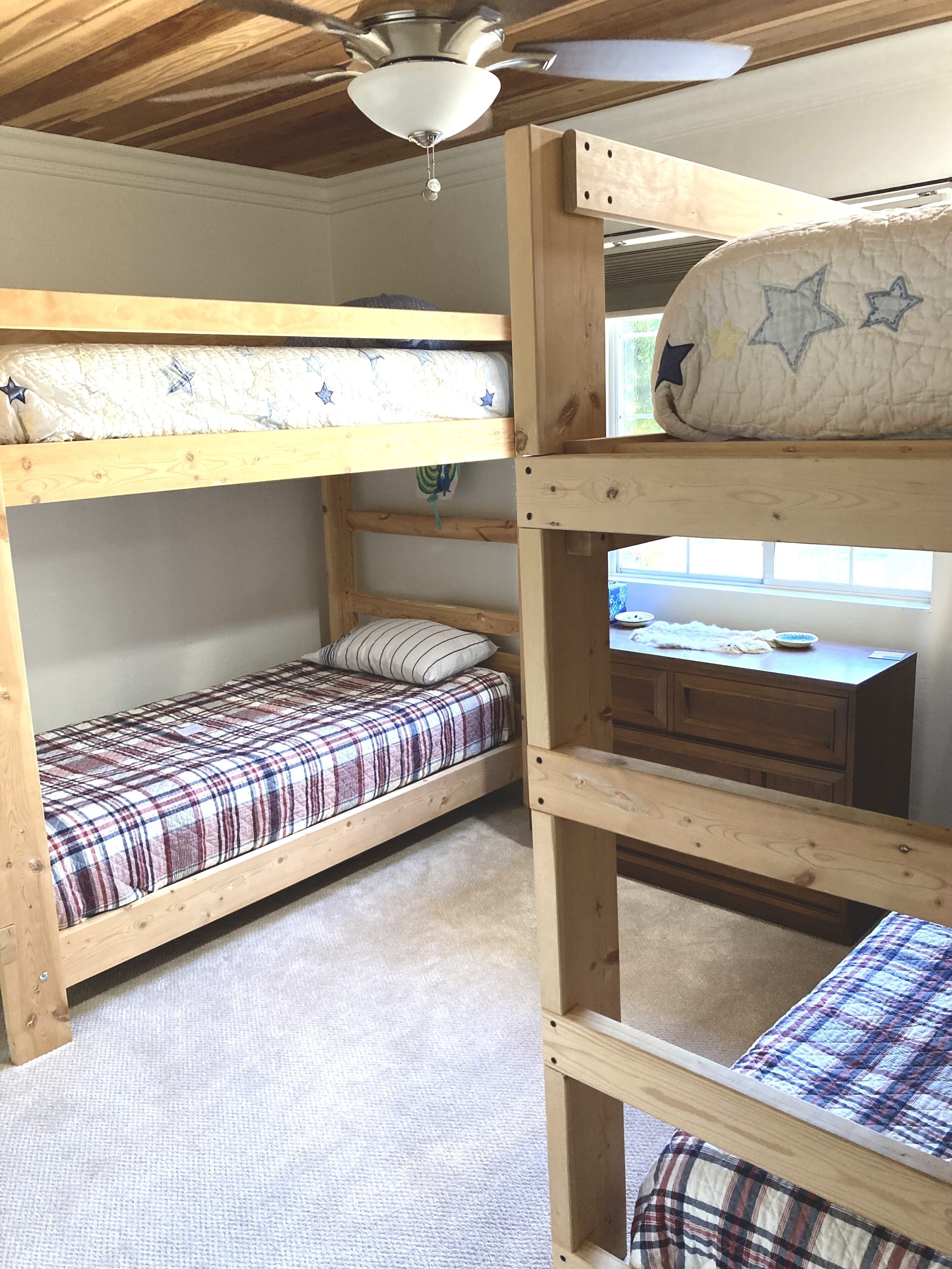 A bunk bed room with a ceiling fan, a window, and a desk with a chair.