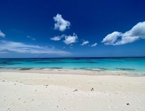 Ein Strand mit klarem türkisfarbenem Wasser und einem weißen Sandstrand unter blauem Himmel mit Wolken.