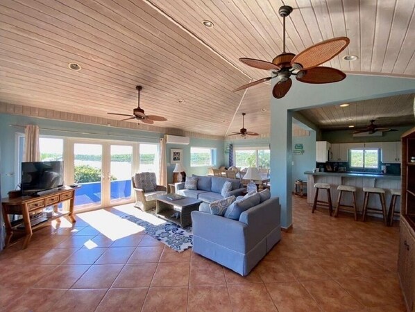 A spacious living area with a large sofa, a television, and ceiling fans.