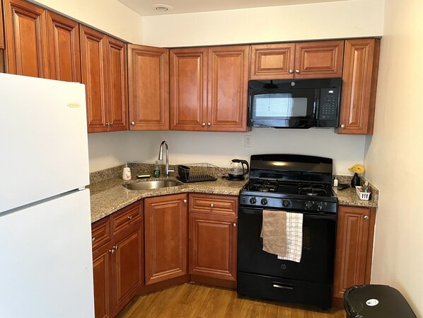 A compact kitchen with wooden cabinets, a stainless steel sink, a black stove, and a microwave above it.