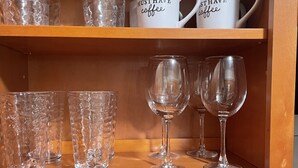 Une étagère de cuisine contenant divers articles en verre, notamment des verres à vin et des verres à cocktail, ainsi que deux tasses blanches avec des inscriptions.