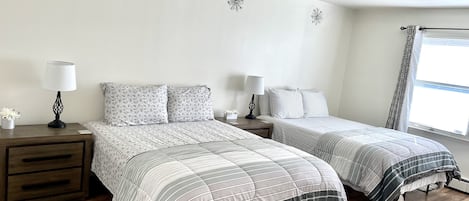 Une chambre avec deux lits, une table de chevet avec une lampe, un plancher en bois et une fenêtre avec des rideaux.